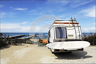 Rear of vintage camper parked on the beach seaside with a surfboard on back - Leisure trip in the summer Stock Photo