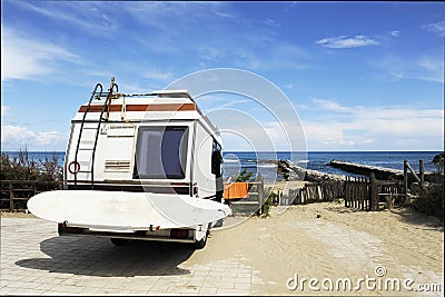 Rear of vintage camper parked on the beach seaside with a surfboard on back - Leisure trip in the summer Stock Photo