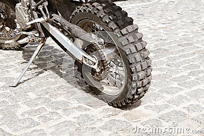 The rear wheel of an off-road motorcycle against the background of a stone pavement. Motorbike parked at empty cobblestone road. E Stock Photo