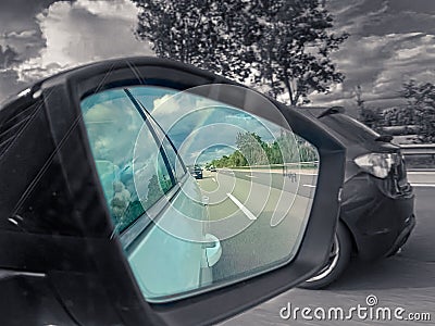 Rearview car driving mirror view at a colorful rainbow while the surrounding is black and white, kind of colorkey. Stock Photo
