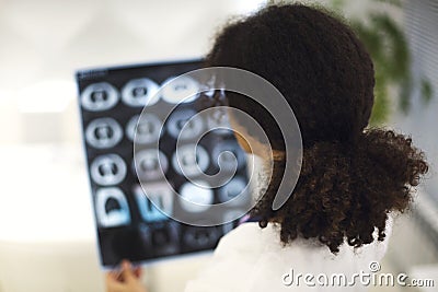 Rearview of ethnic female doctor analyzing X-ray, MRI scan or CT screening while working in hospital Stock Photo