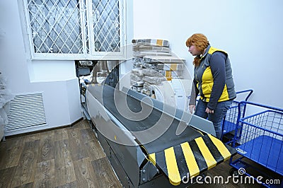 At the receipt and delivery room of post office: postal worker standing by a belt conveyor Editorial Stock Photo