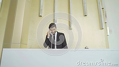 A receptionist or concierge man with uniform at front desk counter in lobby of hotel talking on the phone with guest about the Stock Photo