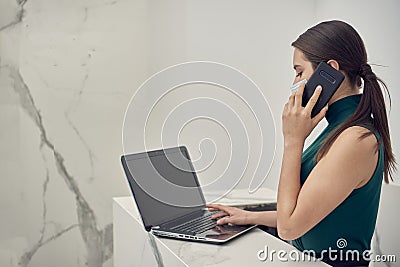 Receptionist making cell phone call while checking his laptop Stock Photo