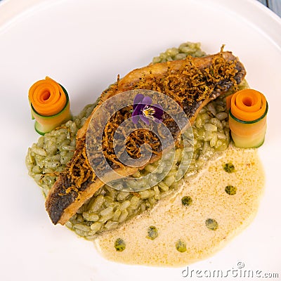 Recipe for fried fillet of sea bass with herb risotto, white wine sauce, fresch creme, roll of carrot and courgette Stock Photo
