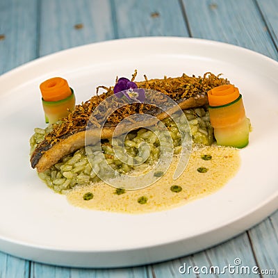 Recipe for fried fillet of sea bass with herb risotto, white wine sauce, fresch creme, roll of carrot and courgette Stock Photo