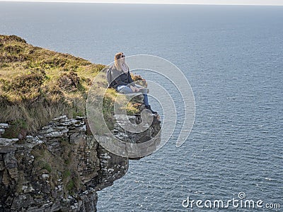 Reckless woman sitting on the edge of a cliff at the Irish west coast Stock Photo