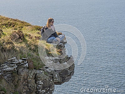 Reckless woman sitting on the edge of a cliff at the Irish west coast Stock Photo