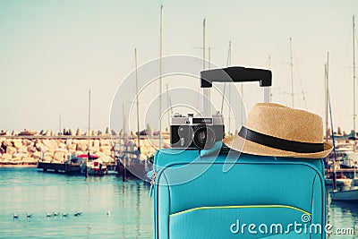 Recreation image of traveler luggage, camera and fedora hat infront of marina with yachts background. holiday and vacation concept Stock Photo