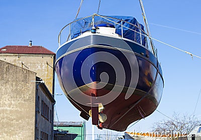 Recreational boat being lifted by heavy industrial crane machinery against blue sky background Stock Photo