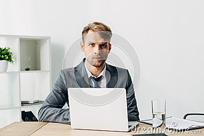 Recruiter looking at camera near laptop and clipboard on table Stock Photo