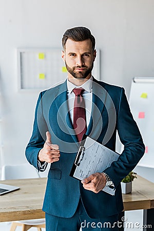 Recruiter standing and holding clipboard with resume letters while showing thumb up Stock Photo