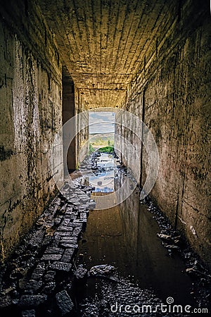 A rectangular flooded tunnel with an exit to mountains. Stock Photo