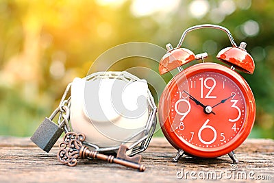 Red alarm clock with piggy bank a key on old wood Stock Photo