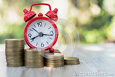 A red alarm clock and a pile of coins resting on the table. Ideas to save money, ideas for business growth, use the right time to Stock Photo