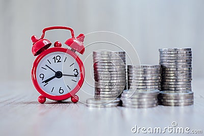 A red alarm clock and a pile of coins resting on the table. Ideas to save money, ideas for business growth, use the right time to Stock Photo