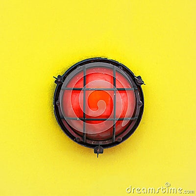 Red alert bulkhead light fixed to a painted yellow orange colour wall background. Photo in square format Stock Photo