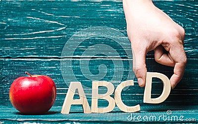Red apple and letters of the ABCD. The hand puts the letter D to the others in a row. Apple for the teacher. Concept of education, Stock Photo