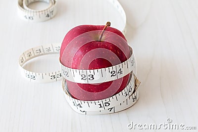 Red apple and measurement tape isolated on melamine wooden plank. Suitable for weight loss diet programme or advertisement. Stock Photo