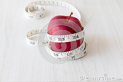 Red apple and measurement tape isolated on white wooden plank. Suitable for weight loss and diet programme advertisement. Stock Photo