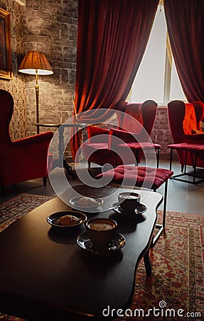 Red armchairs with coffee cups on table in cozy classic interior. Antique living room with red curtains and armchairs. Stock Photo