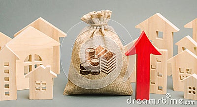 Red arrow up, money bag and miniature wooden houses. The concept of rising property prices. High mortgage rates. Expensive rental Stock Photo