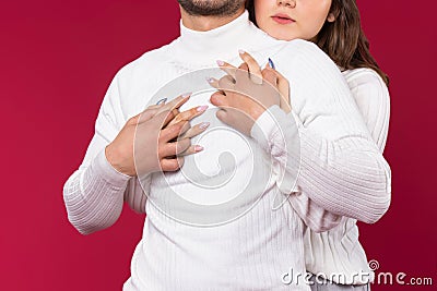 Red background. Enlarged photo of an embrace where girl`s hands hug her soulmate, white sweater. Love on Valentine`s Day Stock Photo