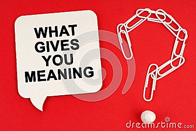 On a red background are a question mark made of paper clips and a sign with the inscription - WHAT GIVES YOU MEANING Stock Photo