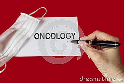 On a red background there is a medical mask and a notepad with the word ONCOLOGY. Medical concept Stock Photo