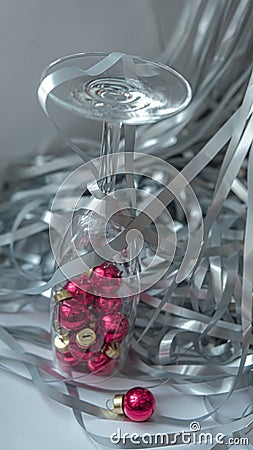 A dynamic composition for a festive mood, consisting of bright red Christmas balls and a transparent sparkling wine glass Stock Photo