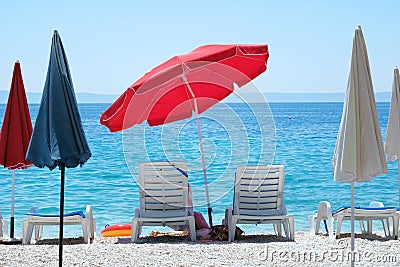 Red beach umbrella and chaise for relax and comfort on sea coast. Happy summer vacations and tourism concept. Paid service on Stock Photo