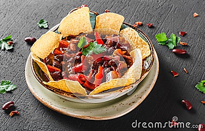 Red bean with nachos or pita chips, pepper and greens on plate over dark background. Mexican snack, Vegetarian food Stock Photo