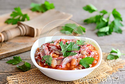 Red bean stew with smoked sausage slices, tomato sauce and fresh parsley in a bowl and on a wooden vintage table Stock Photo