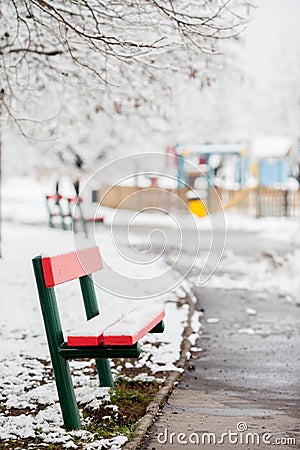 Red bench in a snowy park, children playground in the background Stock Photo