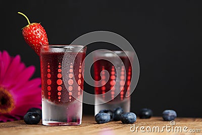 Red berries liqueur in shot glass isolated on black background and wooden table. Homemade alcohol drink concept. Stock Photo