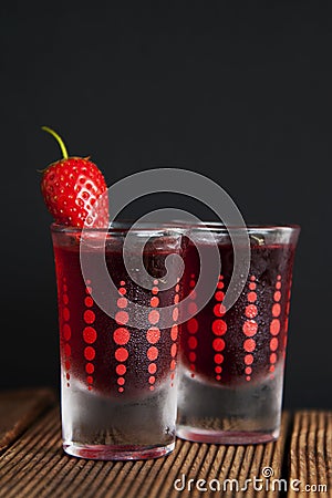 Red berries liqueur in shot glass isolated on black background and wooden table. Homemade alcohol drink concept. Stock Photo