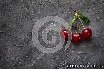 Red berries of ripe cherries with green leaves on a black craft background. Close-up photo of a berry. Stock Photo