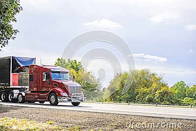 Red big rig semi truck transporting covered semi truck with front wall spoiler running on the road Stock Photo