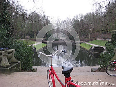 A red bike parked in front of a lake in the Muziekkoepel Noorderplantsoen Park in Groningen, The Netherlands Stock Photo