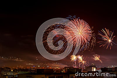 Red blue bright firework in the night sky over a city. Townspeople celebrating the New Year and launching fireworks at midnight. Stock Photo