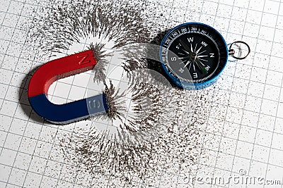 Red and blue horseshoe magnet or physics magnetic and compass with iron powder magnetic field on white paper graph background. Stock Photo