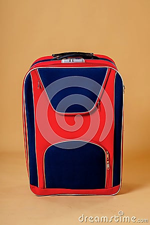 Red with blue stripes travel suitcase with wheels and a telescopic handle on a yellow background Stock Photo