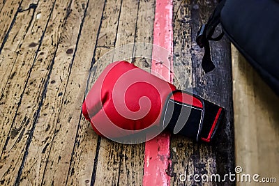 Red boxing glove on the gym floor with wooden covering. Nearby is a black backpack. Sports and training, wrestling and endurance, Stock Photo