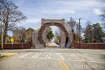 A red brick arch at the entrance of at the Oakland Cemetery with bare winter tree, lush green trees and plants Editorial Stock Photo