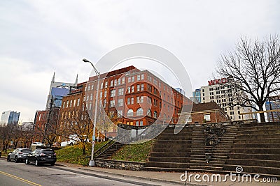 A red brick building surrounded by a staircase, parked cars, tall curved light posts, bare winter trees and skyscrapers Editorial Stock Photo