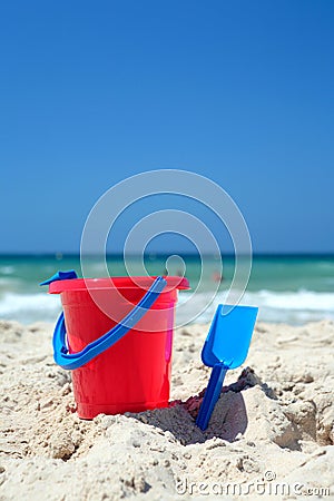 Red bucket and blue spade on sunny, sandy beach Stock Photo