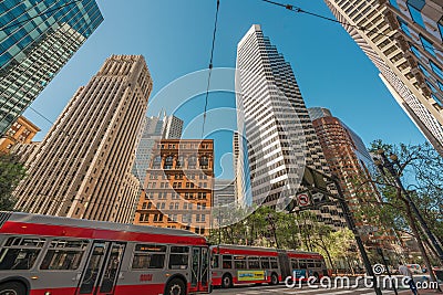 Red buses traverse below the towering mix of modern and classic architecture in San Francisco Editorial Stock Photo