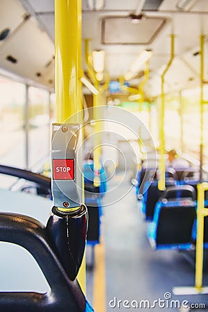 Red button STOP on the bus. Bus with yellow handrails and blue seats. Photo with the sun effect, glare on the lens from the light. Stock Photo