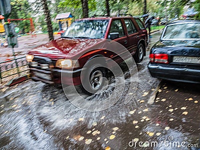 Red car rides in the yard on a wet road in the rain . Beautiful splashes of water from under the wheels. Editorial Stock Photo