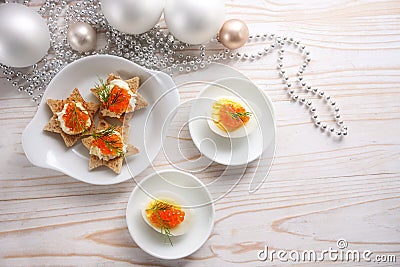 Red caviar on halved eggs and on star shaped canapes, white wooden table with Christmas decoration for a festive holiday buffet, Stock Photo